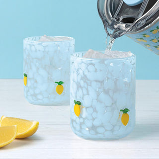 Two glasses with lemon designs being filled with water on a light blue background