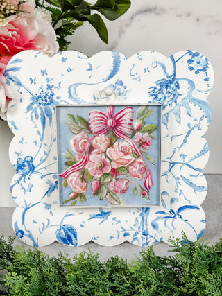 Decorative frame with floral design and pink roses with ribbons on a marble surface.