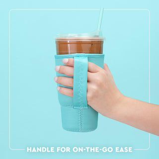 Hand holding a cup with a turquoise sleeve against a light blue background