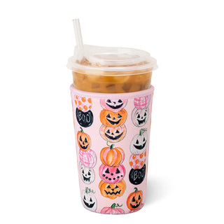 A pink insulated travel tumbler with a clear lid and straw, decorated with a pattern of hand-drawn orange, pink, and white pumpkins and black 'BOO' signs, shown on a white background.