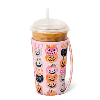 A pink insulated tumbler sleeve with a Halloween pumpkin print, holding an iced coffee in a clear plastic cup with a straw, on a white background.