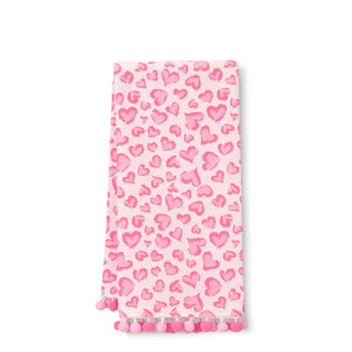 A pink kitchen towel with a watercolor-style heart pattern and pom-pom trim along the bottom edge, shown flat against a white background.