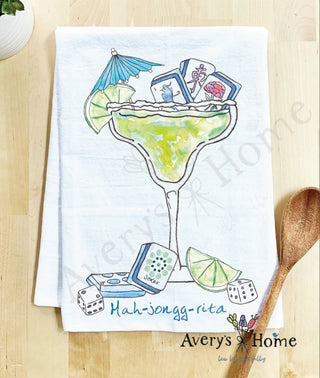 Decorative towel with a margarita design and 'Mah-jongg-rita' text, featuring a wooden spoon on a wooden surface.