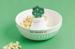 White bowl with popcorn and a cactus-shaped popcorn scoop on a green background