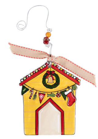 Decorative Christmas ornament shaped like a house with a wreath, bell, and stockings on a white background.