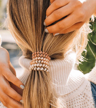 Person styling hair with a beaded hair tie against a blurred outdoor background