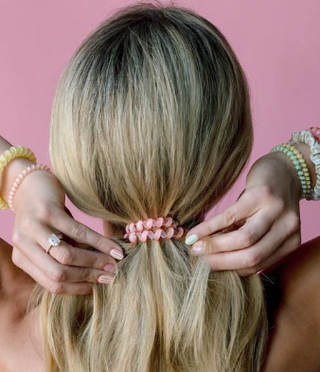 Person styling their hair with a pink scrunchie against a pink background