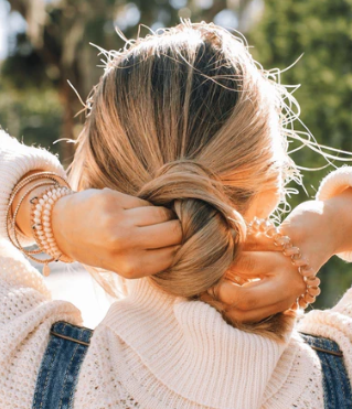 Person braiding their hair with a blurred natural background