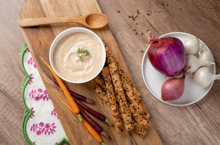Wooden cutting board with breadsticks, dip, and vegetables on a wooden table.
