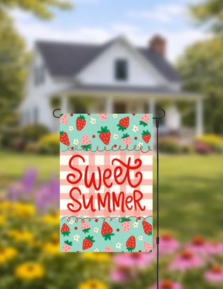 Decorative garden flag with 'Sweet Summer' text and strawberry pattern in front of a house and garden.