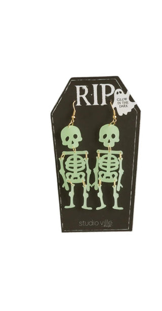 Glowing skeleton earrings on a black card with 'RIP' text, brand 'studio ville' visible.