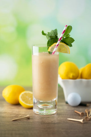 Glass of lemonade with a straw, lemons, and golf balls on a wooden surface.