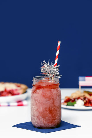 Mason jar with red drink and striped straw on a blue background