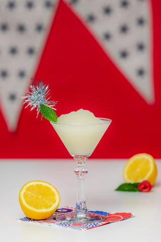 Frozen lemonade cocktail with lemon slices and garnish on a colorful napkin against a red and white geometric background.