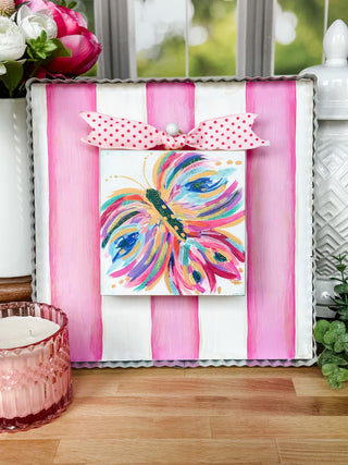 Decorative display board with a colorful butterfly design on a pink and white striped background, placed on a wooden surface.