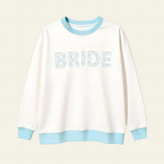 White sweatshirt with 'BRIDE' text and light blue accents on a beige background