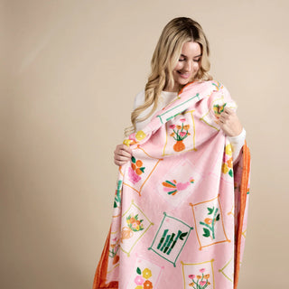 Woman holding a pink floral patterned blanket against a beige background