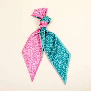 Two patterned scarves, one pink and one blue, tied together on a beige background.