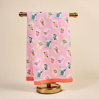 Pink towel with floral patterns hanging on a gold towel rack against a beige background