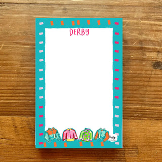 Notepad with colorful clothing illustrations and 'Derby' text on a wooden surface