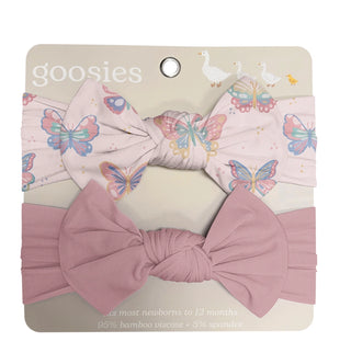 A two-piece baby headband set by Goosies on its original packaging. The set includes a dusty pink twisted headband and a light pink headband with a colorful butterfly and duck print.