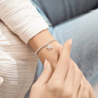Silver bracelet with a flower charm on a wrist against a blurred background