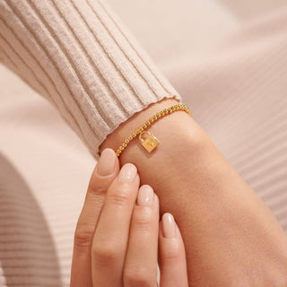 Gold bracelet with a lock charm on a wrist against a neutral background