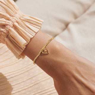 Gold heart-shaped bracelet on a wrist with a soft background