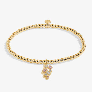 Gold bracelet with a small charm featuring colorful stones on a white background