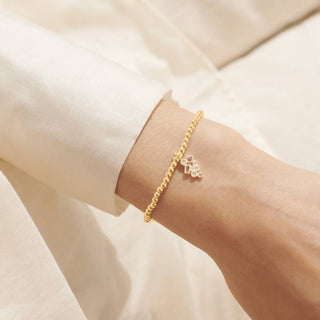 Gold bracelet with a geometric charm on a wrist against a neutral background