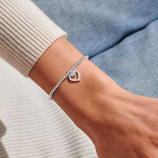 Silver bracelet with a heart charm on a wrist against a neutral background
