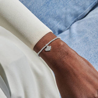 Silver bracelet with a heart charm on a wrist against a blue denim background
