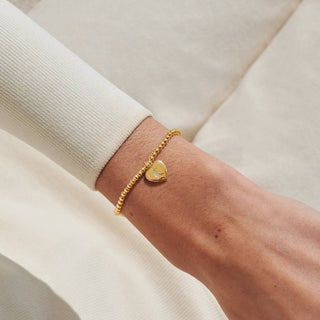 Gold heart-shaped bracelet on a wrist with a neutral background