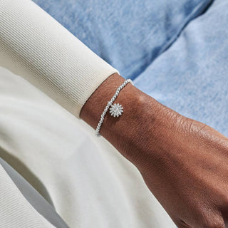 Silver bracelet with a sunflower charm on a wrist against a light blue background