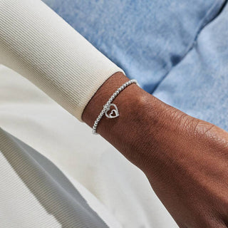 Silver bracelet with a heart charm on a wrist against a neutral background