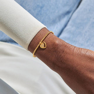 Gold bracelet with a heart charm on a wrist against a light blue and white background