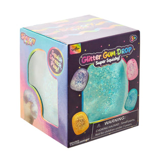 A boxed toy product labeled 'Glitter Gum Drop Super Squishy!' shown on a plain white background. The packaging is predominantly purple with pastel rainbow graphics and a large turquoise glittery gum-drop shape visible through a window on the front.