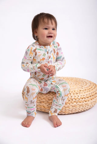 Child wearing a colorful pajama set with animal prints, sitting on a woven stool against a white background.