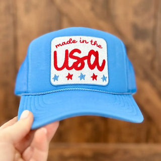 Blue cap with 'made in the USA' patch held by a hand against a wooden background
