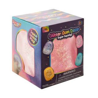 A boxed toy product labeled 'Glitter Gum-Drop Super Squishy!' shown on a plain white background. The packaging is dark purple with colorful pastel graphics, a window showing a pink glittery squishy material, and several illustrated glitter eggs around the front.