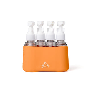 Set of six small bottles with white caps in an orange holder labeled 'En Route' on a white background