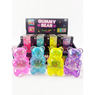 Four translucent gummy bear toys filled with glitter in pink, blue, yellow, and purple, displayed in front of a black retail box labeled 'GUMMY BEAR' on a white background.