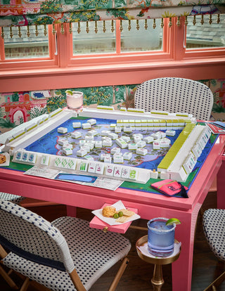 Pink dining table with a large mahjong game set up, surrounded by chairs in a room with colorful walls.