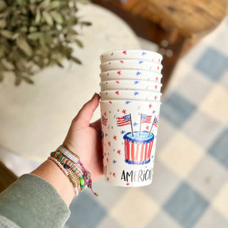 Hand holding a stack of plastic cups with American flag design on a checkered floor.