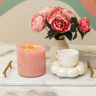 Pink candle, white mug, and vase with pink flowers on a marble surface.