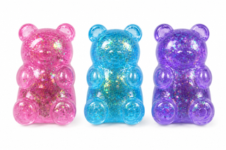 Three translucent gummy bear figurines filled with glitter, shown side by side in pink, blue, and purple on a white background.