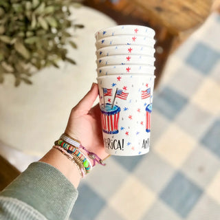 Hand holding a stack of plastic cups with American flag design on a checkered surface.