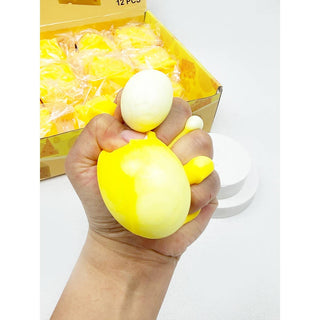 Hand holding a yellow stress ball with a box of similar balls in the background.
