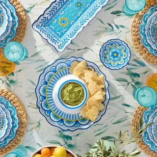 Dessert platter with cookies, fruit, and a bowl of green sauce on a decorative tablecloth.