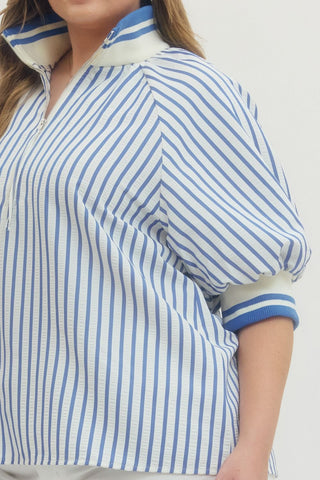 Person wearing a blue and white striped jacket with a high collar on a plain background